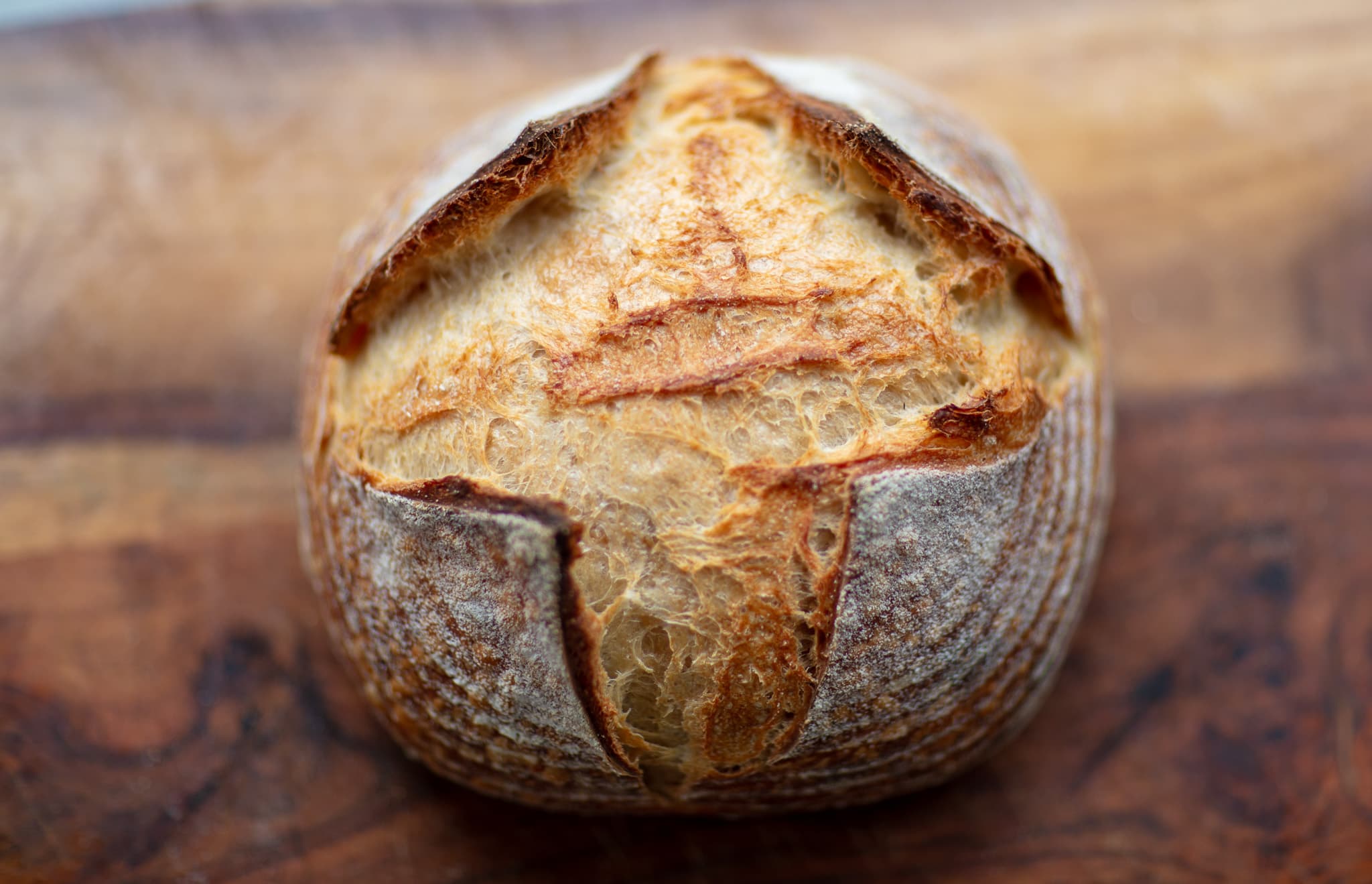 A close view of a tall sourdough boule opening dramatically along its scored crust.