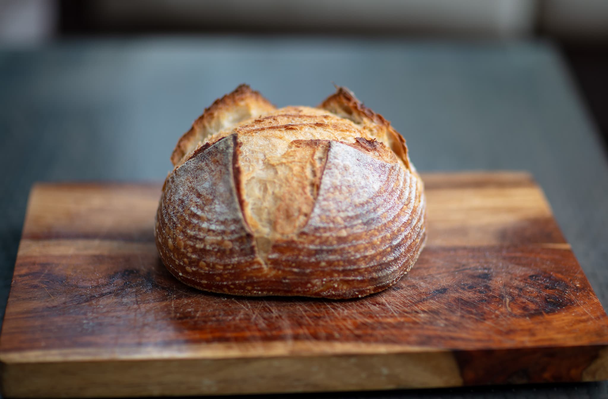 A golden sourdough boule with a deeply opened score, centered on a wooden bread board.