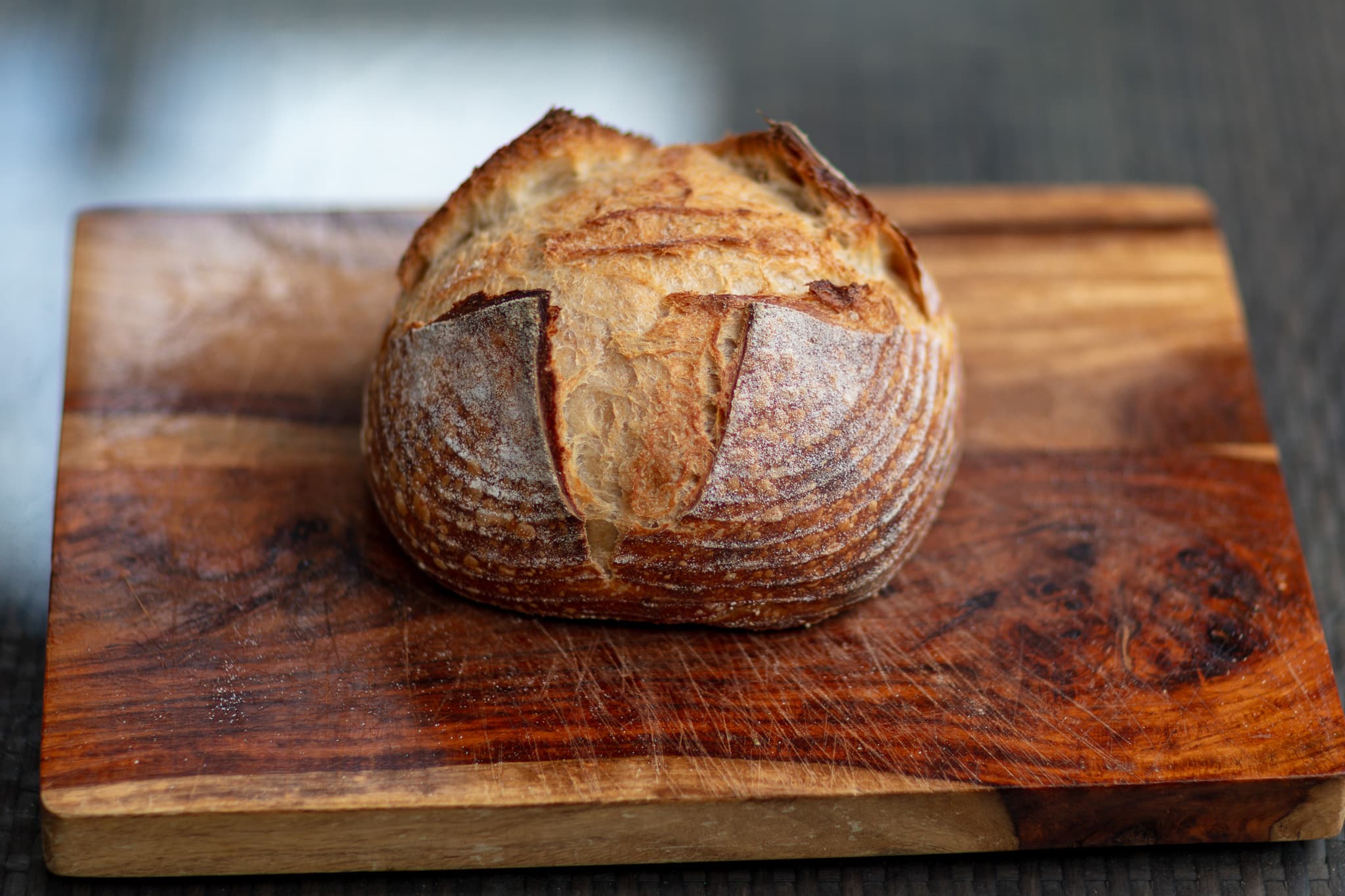 A sourdough boule with flour-dusted scoring on a wooden cutting board.