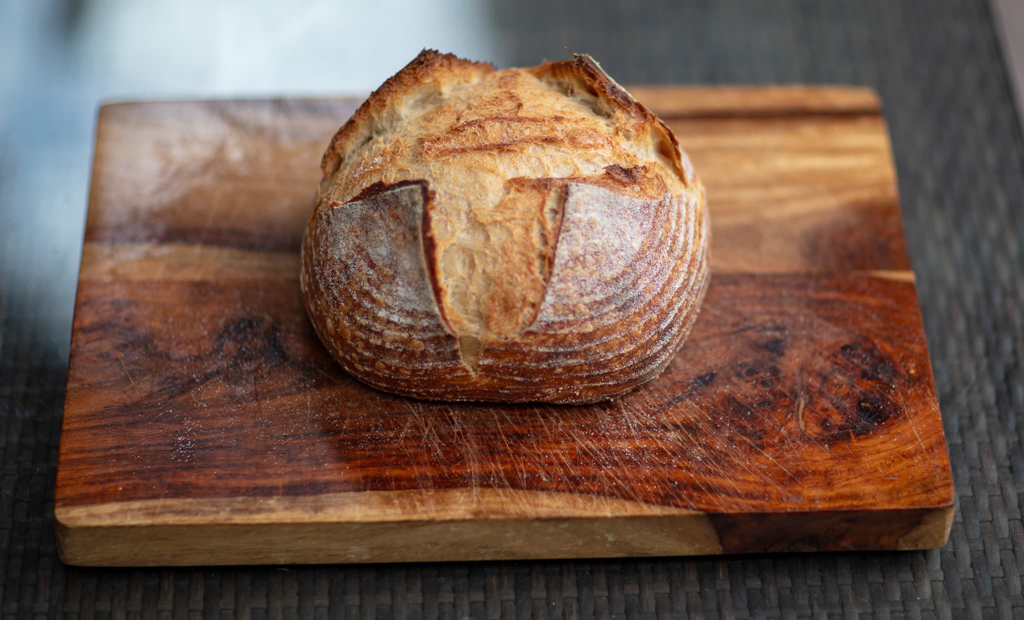 A golden sourdough boule centered on a well-used wooden bread board.