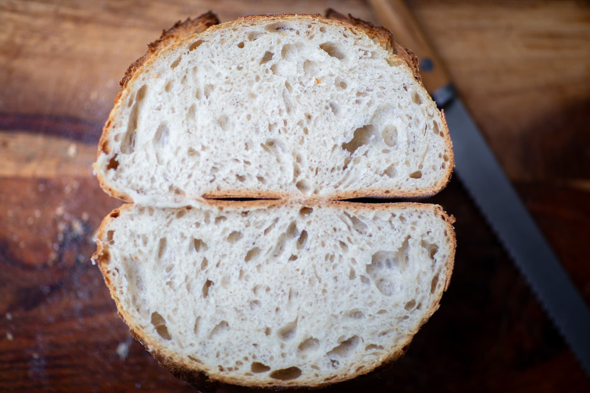 A sourdough loaf cut open to reveal a translucent, irregular crumb beneath a dark, blistered crust.